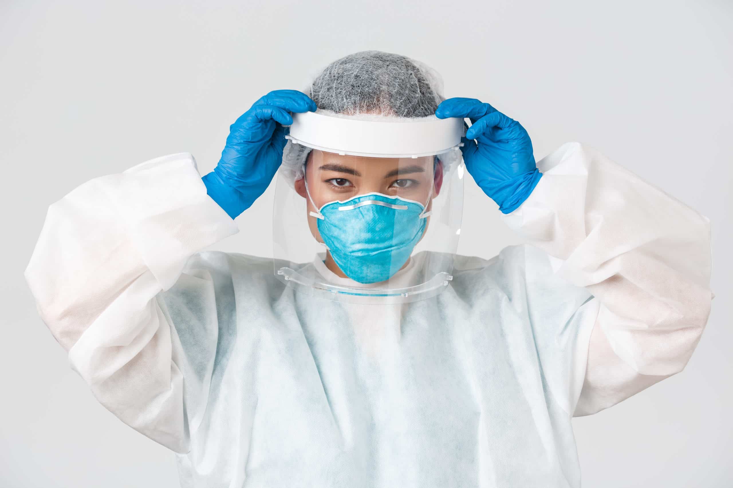 Covid-19, coronavirus disease, healthcare workers concept. Confident serious-looking asian female doctor, put on face shield and personal protective equipment before entering contagious zone.
